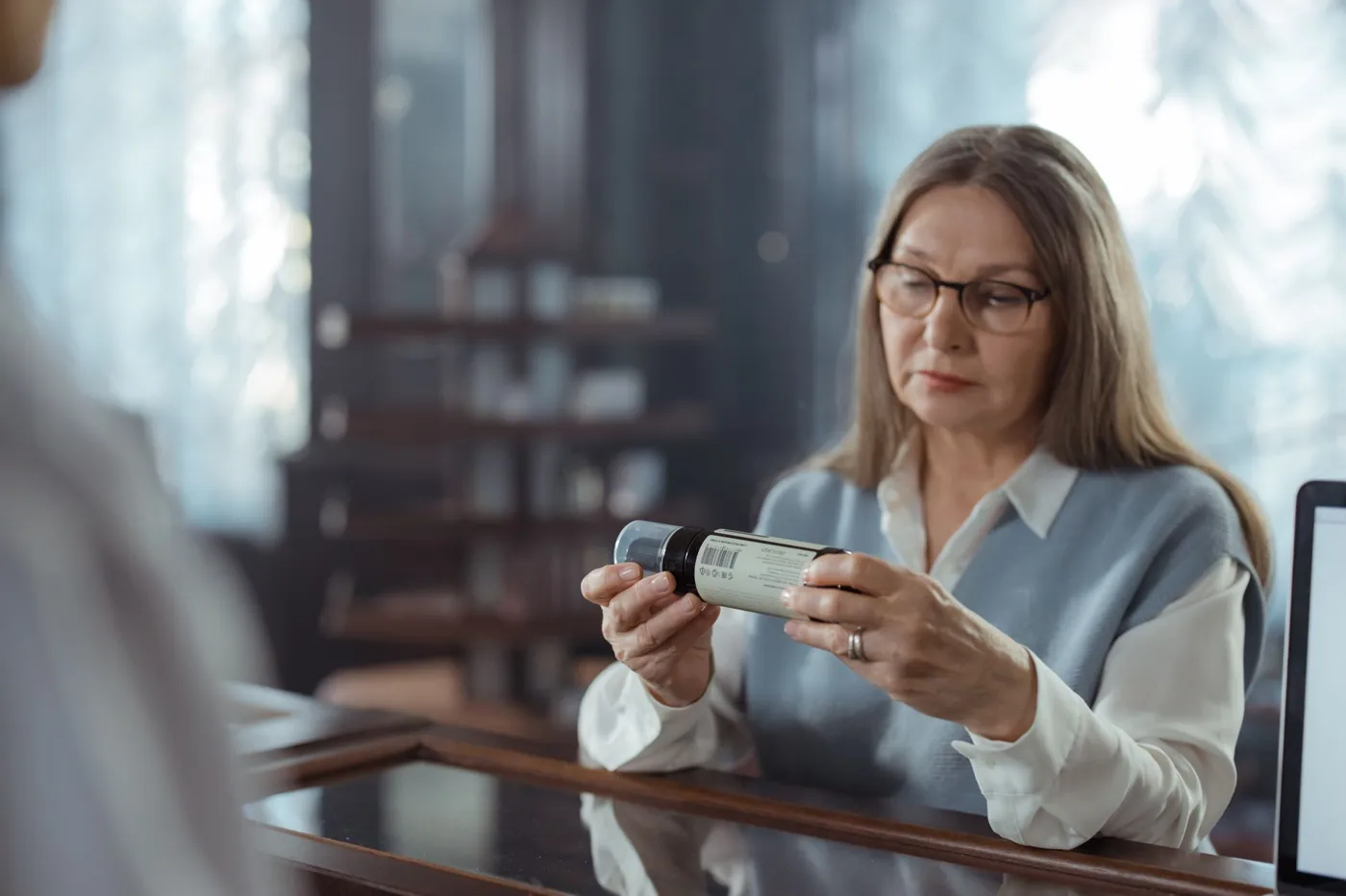 Woman with glasses reading the label on a supplement bottle
